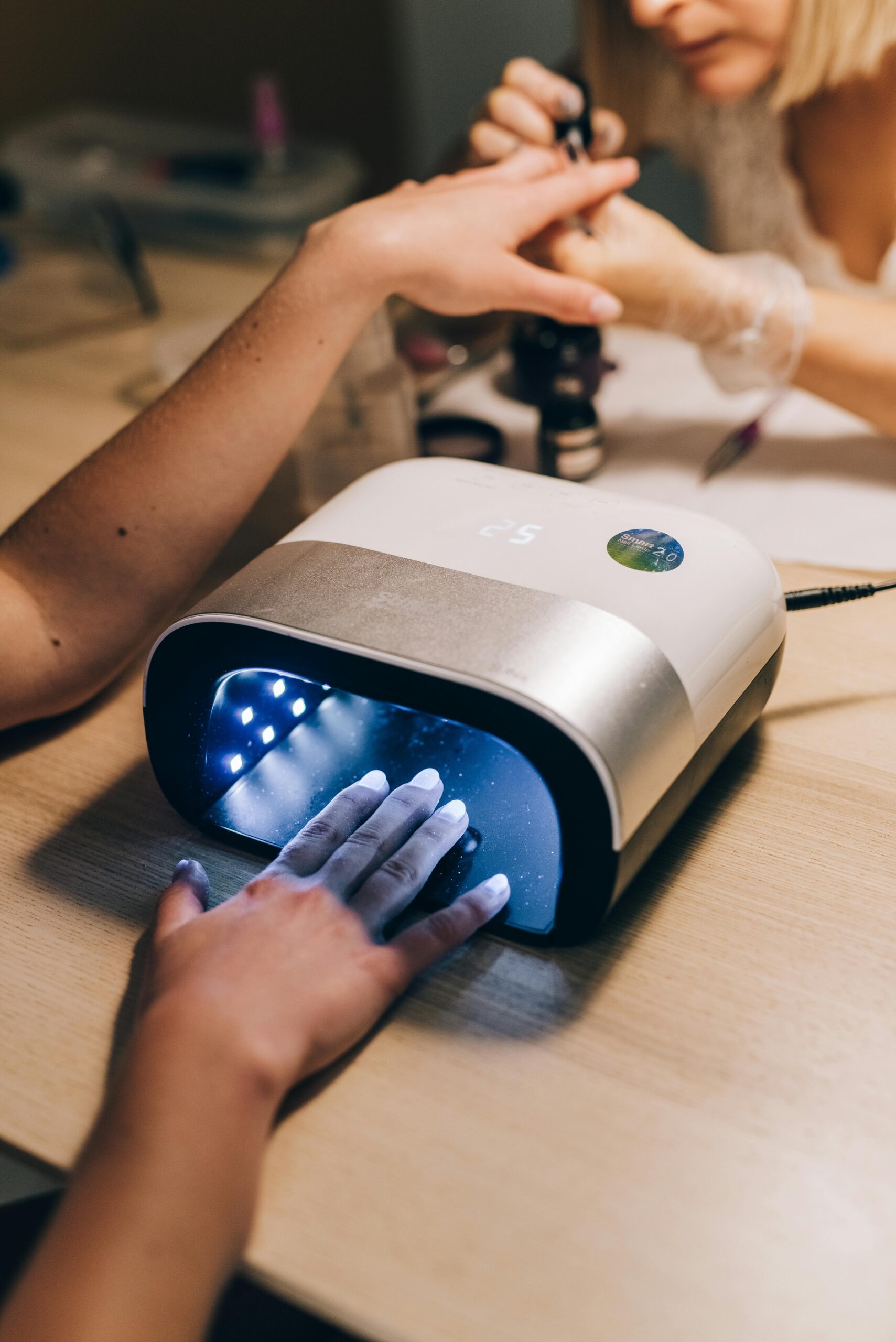 Close-up of a professional manicure using a nail dryer in a salon setting.